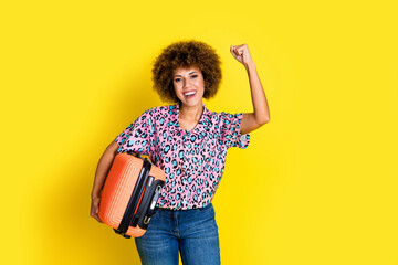 Photo of positive lucky woman wear animal print shirt rising fist holding luggage isolated yellow...