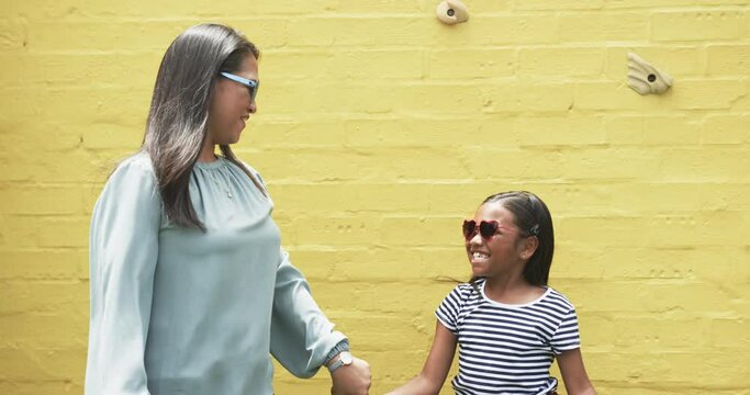 Biracial mother and daughter in sunglasses dancing against yellow background outdoors