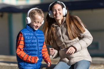 A mother at her little son enjoy listening to music with white headphones
