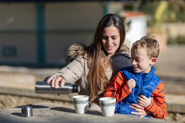  A smiling mother serves her young son a hot chocolate, in a picnic area