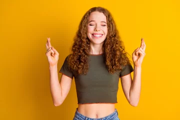 Deurstickers Photo of cheerful dreamy lovely girl wear trendy khaki clothes showing hands with crossed fingers isolated on yellow color background © deagreez