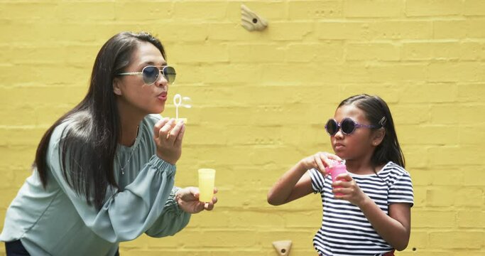 Biracial mother and daughter in sunglasses blowing bubbles