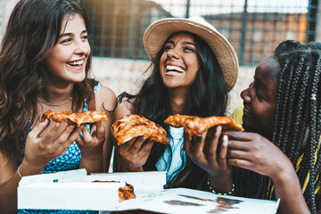 Three young female friends eating pizza sitting outside - Happy women enjoying street food in the...