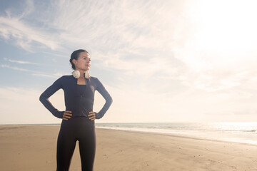 Female runner on beach with hands on hips against blue sky