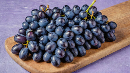 Fototapeta premium Large bunch of purple organic grapes on wooden cutting board. Ripe, delicious and healthy fresh fruits of autumn, symbol of abundance on rustic wood background. Copy space.