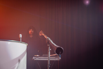 A DJ booth with a hooded figure adjusting equipment, microphone stand in the foreground, ambient...