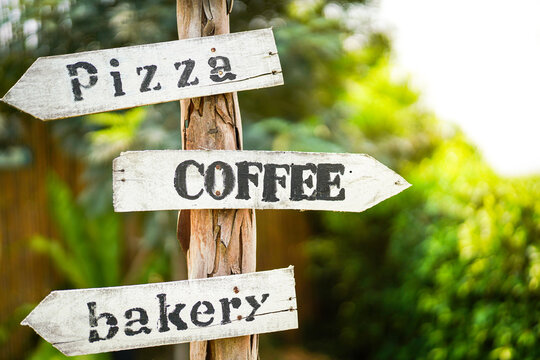 "Coffee, pizza and bakery" wooden plate sign in English with arrow pointing to the left and right. Sign and symbol for food restaurant cafe. Close-up.