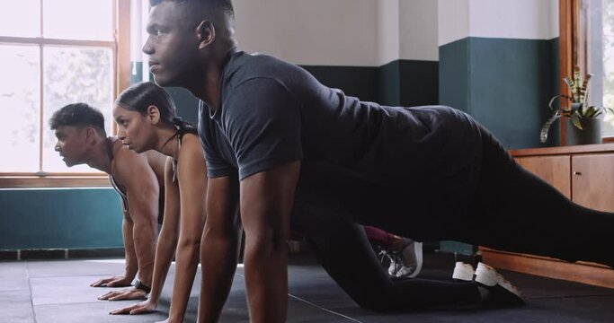 A man and a woman workout together in a gym, doing push ups and squats with a group of people. They sit and engage in floor exercises as part of their intense workout routine
