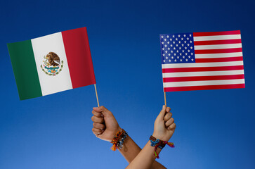 People's hands holding the national flag of Mexico and EE.UU., USA. waving on a blue background.	