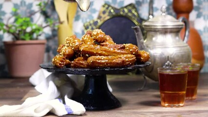 woman pouring a honey sirup on algeria oriental Balah el sham dessert fritters named zlabiat al banan in algerian language with arabic tea