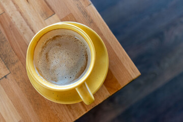Golden elixir. Yellow cup macchiato, served on brown wooden table,  shot from above. Morning ritual.