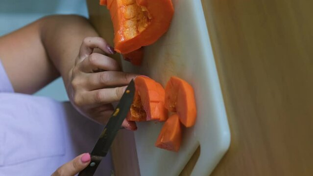 Vertical video. Close-up of Female cutting papaya on chopping board indoors in the kitchen, slow motion