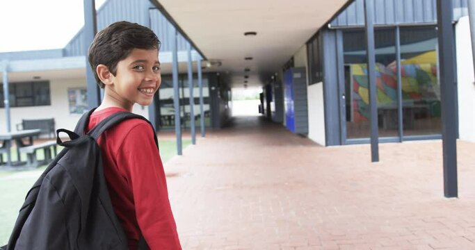 In a school corridor, a young Caucasian student smiles over his shoulder with copy space