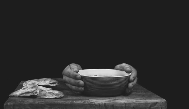 Hands holding a bowl with bread on the side. Food, hunger, charity feeding, poverty concept image, symbolising a dark and homeless society. Black background. copy space. Salvation Army. Soup kitchen.