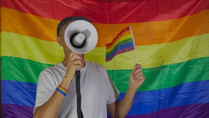 Unrecognizable gay person holds megaphone and rainbow flag. LGBT rights concept