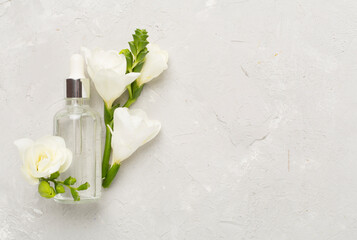 Cosmetic bottle with flowers on concrete background, top view