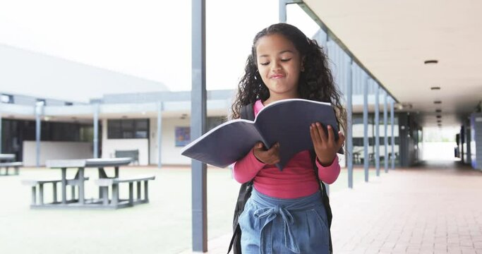 In a school corridor, a young biracial girl is engrossed in reading a book