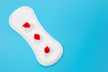 Feminine hygiene pad with red flowers on pink background. First menstrual period concept,...