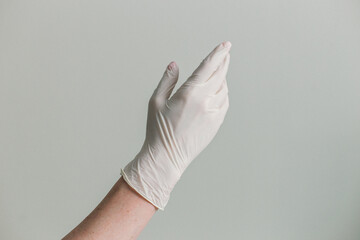 The person is donning a pair of white latex gloves, covering their hands from wrist to fingertip, with each thumb secured in its own sleeve