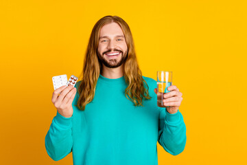 Photo of friendly positive man toothy smile hold glass fresh water pills isolated on yellow color background - obrazy, fototapety, plakaty