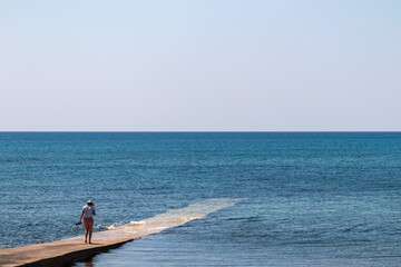 Tourist woman walking on concrete pier in the waters of Adriatic Sea in coastal town Medulin,...