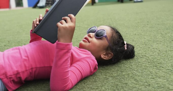 In a school setting, a young biracial student lies on the grass