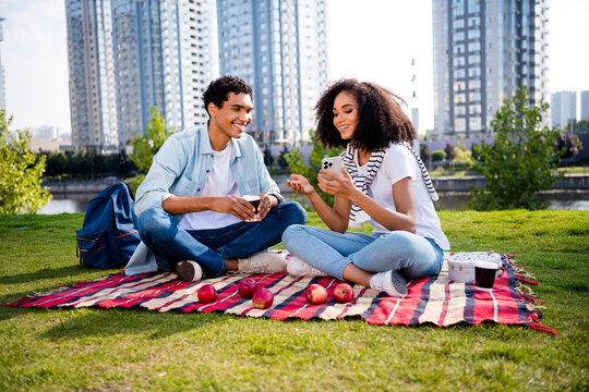 Full body photo of two beautiful people sit blanket drink coffee use smart phone sunshine megapolis outdoors