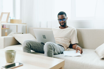 Happy African American freelancer working on a laptop in a modern living room The young black man...