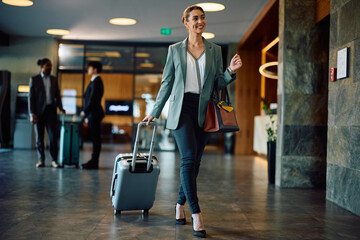 Happy businesswoman with travel bag arriving at hotel. - obrazy, fototapety, plakaty