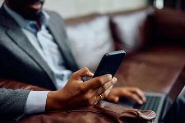 Close up of black businessman using cell phone while working on laptop.