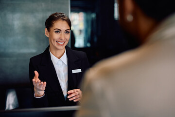 Happy hotel manager talking to  guest at reception desk.