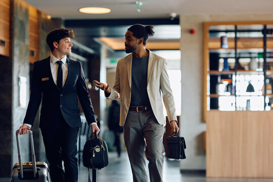 Happy receptionist and black man communicating while walking through hotel hallway.