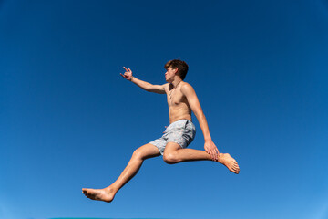 Fototapeta premium A happy young man jumps and dances against a backdrop of blue sky on a summer day.