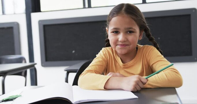 In a school setting, a young biracial student sits at a desk