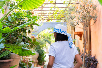 Woman from behind with a hat walking through a lush and extraordinary garden full of plants where...
