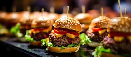 Several hamburgers on black tray with lettuce, tomato, cheese