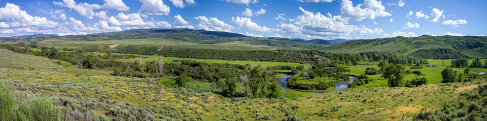 Fototapeta na wymiar Panoramic view of valley with river bend, green grass, mountains and cloudy blue sky near Deal Gulch from the route CO-317 W. Colorado