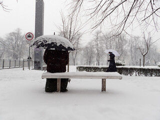 Heavy snowfall in the city. People walking in the streets. Trees and branches covered in white....