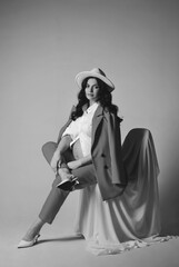 Black and white portrait of brunette pregnant woman in white hat, shirt and red suit posing on a cyclorama. The concept of stylish motherhood