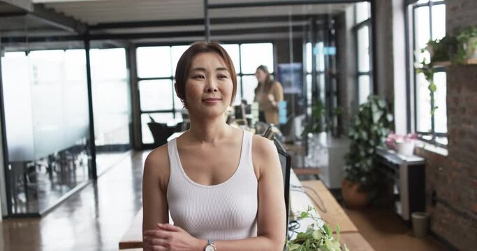 An Asian woman stands confidently, arms crossed, in a casual business office