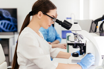 Medical Research Scientist Looks at Biological Samples Under Digital Microscope in Applied Science Laboratory. Beautiful Caucasian Lab Engineer in White Coat Working on Vaccine and Medicine
