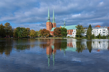Lubeck, Germany. View of Lubeck Cathedral from the opposite shore of Muhlenteich (Mill pond) in autumn day. The cathedral was started in 1173 and consecrated in 1247. - 764266394