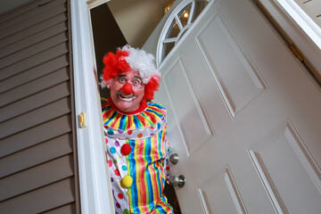 Awkward creepy man dressed in a clown costume answering the door during Halloween - obrazy, fototapety, plakaty