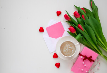 Bouquet of red tulips, gift boxes with ribbon bows, cup of coffee and greeting card on white table top view. Beautiful spring breakfast on Mothers or Women's International day 8 march.