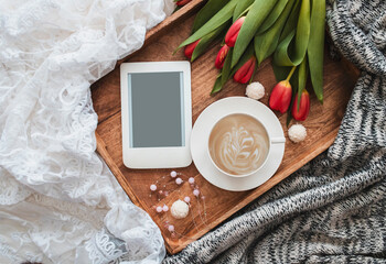 Romantic composition with cup of coffee, red tulips and e-reader with copy space on wooden tray....