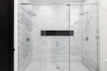 A large, luxury double shower with marble subway tile walls, marble hexagon floor, and black...