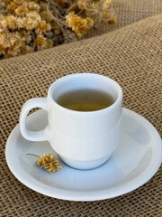 A cup of hot tea made with Macela (Achyrocline satureioides) flowers on a wooden background. Macela flower, medicinal plant, natural, in Brazil.