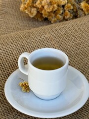 A cup of hot tea made with Macela (Achyrocline satureioides) flowers on a wooden background. Macela flower, medicinal plant, natural, in Brazil.