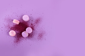 Obraz na płótnie Canvas Pastel colored sweet french macaroons and splash of dry blueberry powder on purple background. Beautiful composition for bakery and pastry shop. Top view with copy space for text