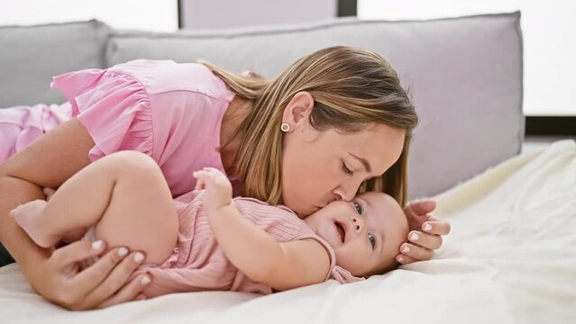 Joyous mother lying on sofa, kissing happy daughter at home in living room, sharing a lovely lifestyle